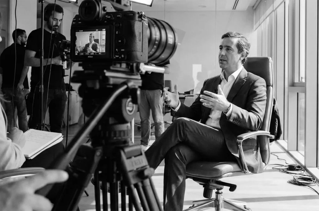 Diretor de empresa a ser entrevistado por equipa de produção de vídeo corporativo em Lisboa, com câmara profissional e luz de três pontos